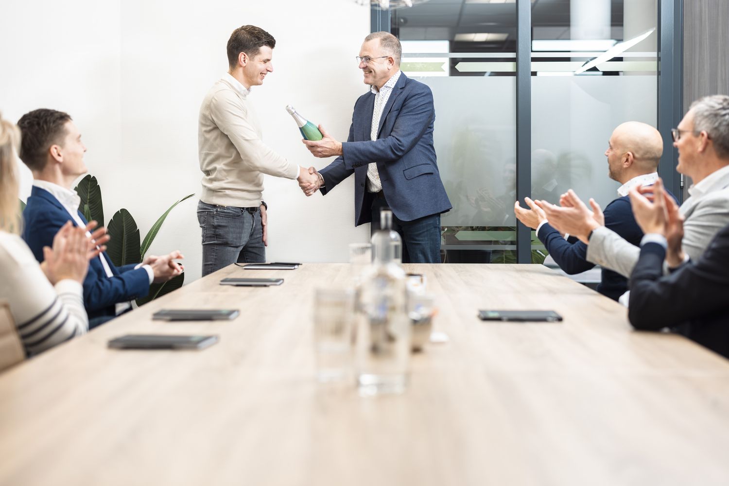 Een groep applaudisseert na een sessie rond de vergadertafel